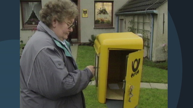 Eine Frau leert einen Postbriefkasten vor ihrer Haustür