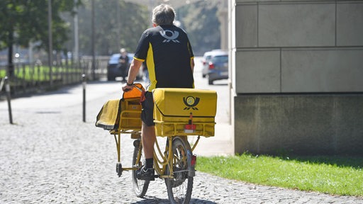 Ein Postbote fährt bei sommerlichen Temperaturen mit dem Fahrrad
