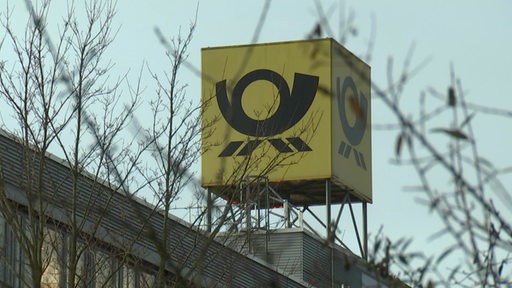 Ein Schild mit dem Logo der Deutschen Post hinter Baumzweigen.