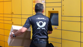 Ein Mitarbeiter der Deutschen Post nimmt ein Paket aus einer DHL-Packstation.