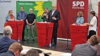 Mehrere Politiker stehen bei einer Pressekonferenz auf einem Podium.