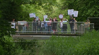 Mehrere Personen stehen auf einer Brücke und halten Schilder in die Höhe.