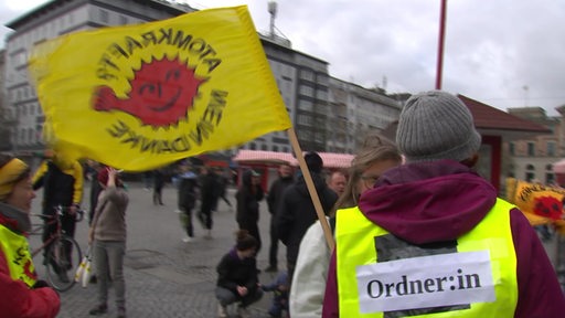 Eine Gruppe von Leuten demonstriert am bremer Hauptbahnhof  mit Flaggen und Bannern gegen den Castor-Transport.