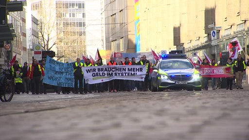 Teilnehmer einer Demonstration tragen Warnwesten und laufen mit Bannern hinter einem Polizeiauto her