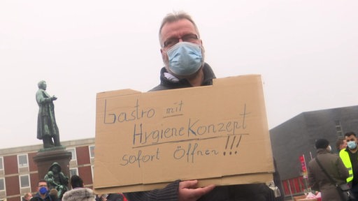 Ein Mann der ein Schild während eines Protests in der Hand hält mit der Aufschrift "Gastro mit Hygienekonzept sofort öffnen".