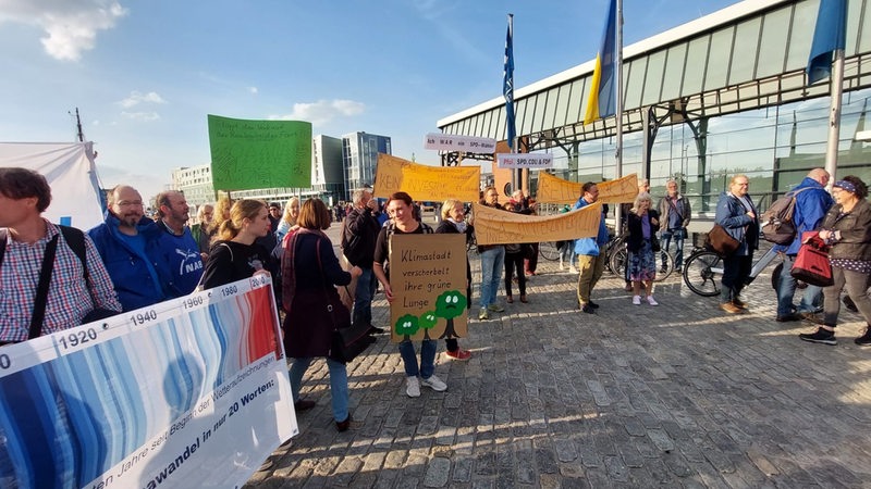 Menschen stehen mit Plakaten vor einer Halle.