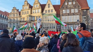 Menschen schwenken iranische Flaggen auf dem Bremer Marktplatz.