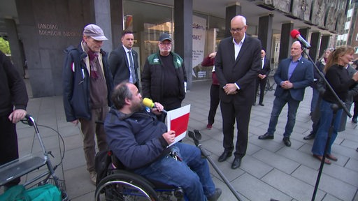 Der Demo-Redner im Rollstuhl überreicht dem Bürgermeister Andreas Bovenschulte eine Mappe mit ihren Forderungen.