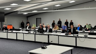 In einer zu einem Gerichtssaal umfunktionierten Halle sitzen mehrere Menschen.