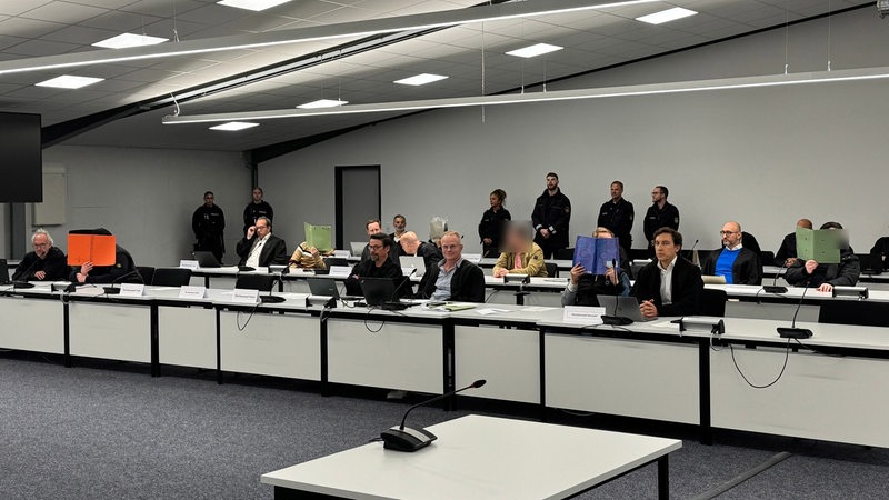 In einer zu einem Gerichtssaal umfunktionierten Halle sitzen mehrere Menschen.