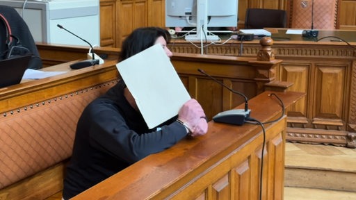 Der Angeklagte versteckt sein Gesicht hinter einem weißen Papier vor Gericht.