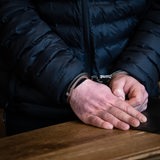 Die Hände eines Mannes sind mit Handschellen gefesselt und liegen auf einem Tisch.