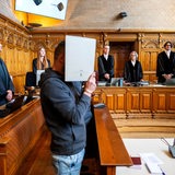 Zwei Angeklagte stehen vor ihren Anwälten im Gerichtsaal. 