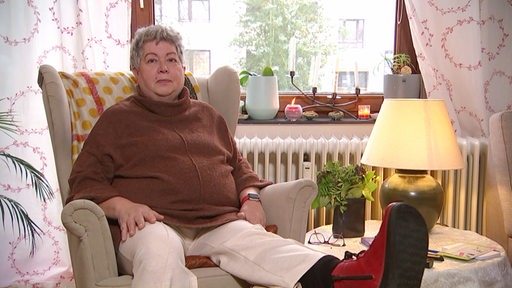 Eine Frau sitzt in einem Wohnzimmer auf einem Sessel.