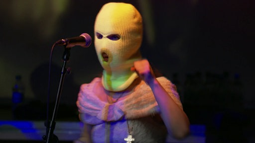 Eine Sängerin von Pussy Riot bei einem Auftritt. Sie trägt eine Strickhaube.