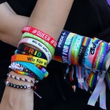 Eine Frau zeigt ihre Arme mit verschiedene queere Armbänder und Bändchen (Symbolbild)