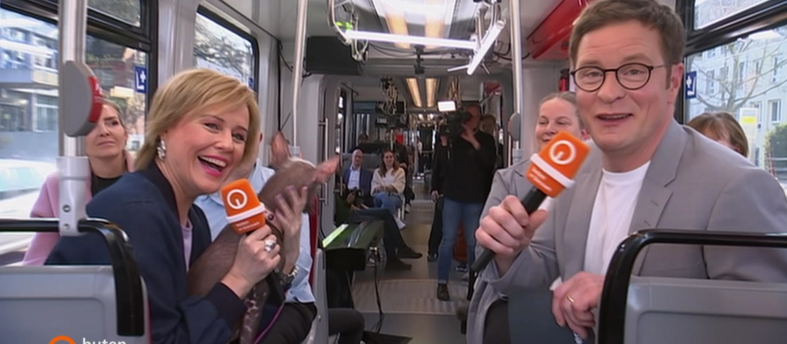 Kirsten Rademacher und Felix Krömer moderieren eine Sendung in einer Straßenbahn.