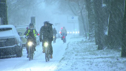 Ein zugeschneiter Fahrradweg. Auf dem Weg Fahradfahrer mit leuchtenden Lichtern.