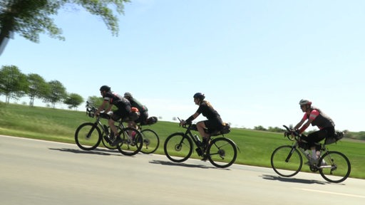 Rennradfahrer und -fahrerinnen auf einer Straße bei einem Rennen mit strahlendem  Sonnenschein. 