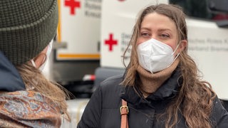 Eine Frau mit FFP2 Maske steht vor einem Fahrzeug vom Roten Kreuz
