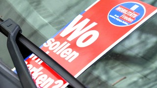 Ein Flyer mit dem Text "Wo sollen wir parken" klemmt unter einem Scheibenwischer