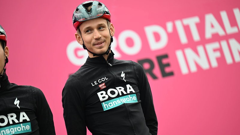 Radsportler Lennard Kämna steht lächelnd bei der Teampräsentation vor dem Start einer Giro-Etappe auf dem Podium.