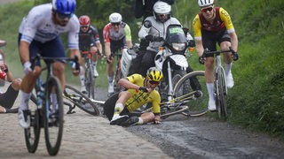 Der Bremer Radprofi Niklas Behrens hockt nach einem Sturz beim Rennen Paris-Roubaix auf dem Kopfsteinpflaster, ein weiterer Fahrer war ebenfalls gestürzt, andere sind von den Rädern abgestiegen.