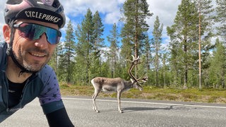 Extrem-Radsportler Florian Schigelski posiert auf dem Rad während der Fahrt mit einem Elch auf der Straße am Nordkap.