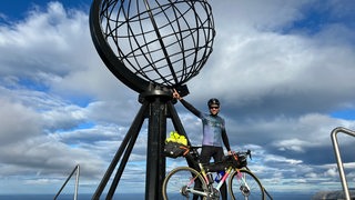 Extrem-Radsportler Florian Schigelski posiert triumphierend mit seinem Rad am Aussichtspunkt am Nordkap.