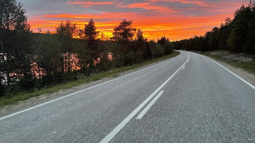 Blick auf eine Straße in Schweden mit einem orange-gelben Sonnenuntergang am Horizont.