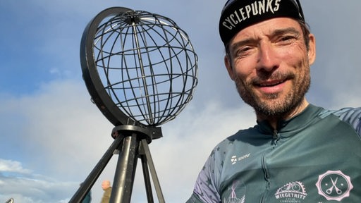 Extremradsportler Florian Schigelski posiert strahlend am Nordkap-Aussichtspunkt.