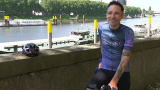 Der Bremer Radsportler Florian Schigelski steht lächelnd beim Interview am Weserufer.
