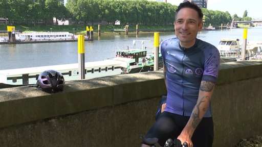 Der Bremer Radsportler Florian Schigelski steht lächelnd beim Interview am Weserufer.