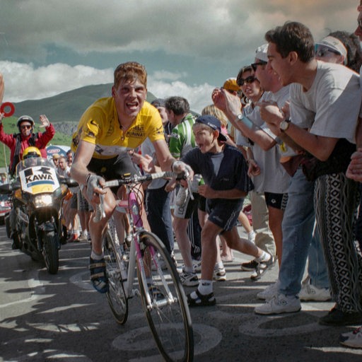 Jan Ullrich kämpft sich im Gelben Trikot bei der Tour de France 1997 einen Berg hoch, angefeuert von Fans am Wegesrand.
