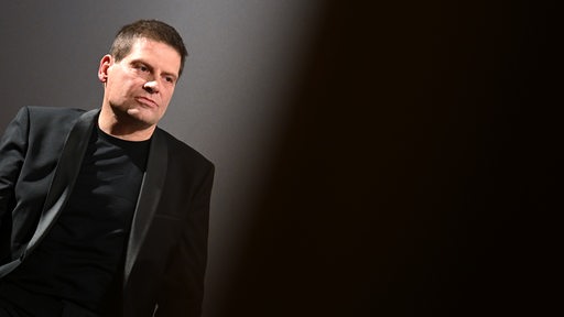 Der ehemalige Radprofi Jan Ullrich nachdenklich im schwarzen Anzug vor einem schwarzen Hintergrund bei einer Kinopremiere.