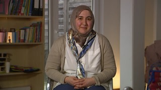 Die Sozialassistentin Rahaf Moselli trägt ein Kopftuch, sitzt auf einem Stuhl und lächelt.