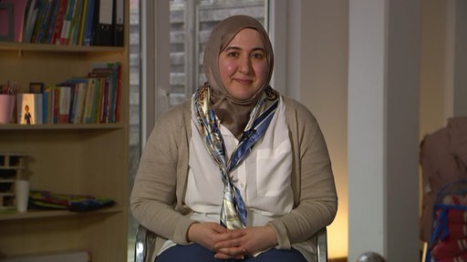 Die Sozialassistentin Rahaf Moselli trägt ein Kopftuch, sitzt auf einem Stuhl und lächelt.