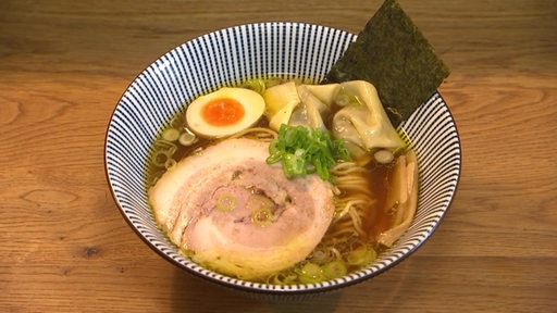 Eine Ramen Suppe mit Fleisch und Ei in einem Teller serviert.