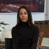 Eine Frau mit dunklen Haaren und dunklem Pullover blickt in die Kamera.