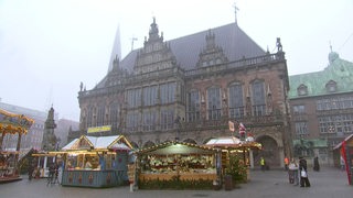 Das Rathaus in der Bremer Innenstadt ist in Nebel eingeschleiert. Vor dem Rathaus stehen ein paar Weihnachtsmarktbuden.