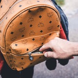 Eine Hand greift in die Vordertasche eines Rucksacks einer anderen Person