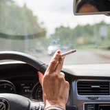 Hand einer Frau mit brennender Zigarette im Auto.