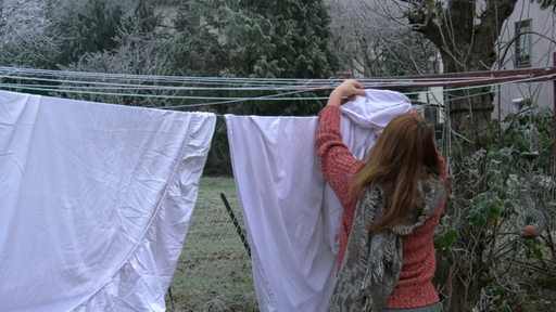 Eine Frau hängt bei Kälte draußen Wäsche auf.