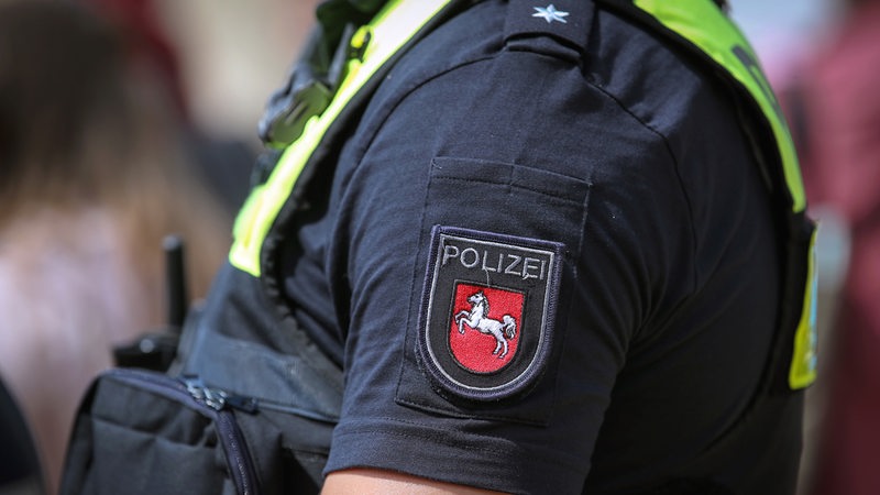 Polizist mit Warnweste und Logo des Bundesland Niedersachsen während einer Razzia (Symbolbild)