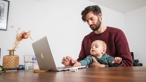 Ein Vater sitzt mit seinem Kleinkind im Home Office.