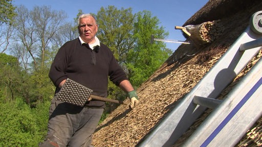 Der Reetdachdecker Marius Schmidtke mit einem Werkzeug auf einem Dach.