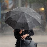 Eine Frau läuft mit einem Schirm durch einen Regenschauer.