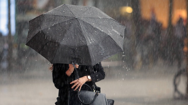 Eine Frau läuft mit einem Schirm durch einen Regenschauer.