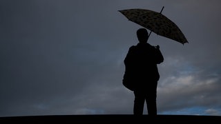 Ein Mensch läuft mit einem Regenschirm vor einer dunklen Wolkenfront. 