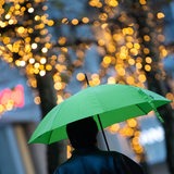 Ein Fußgänger läuft mit einem grünen Regenschirm durch eine weihnachtlich beleuchtete Straße.